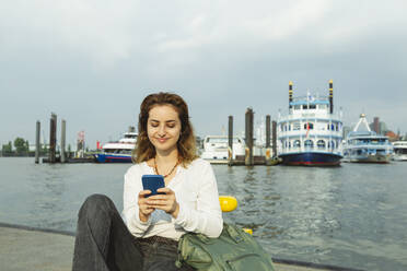 Lächelnde Frau mit Smartphone im Hamburger Hafen, Deutschland - IHF01241