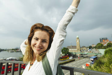 Glückliche Frau mit erhobenem Arm an einem Geländer stehend, Hamburg, Deutschland - IHF01257
