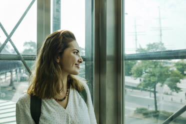 Lächelnde Frau schaut durch Glas im Aufzug - IHF01259