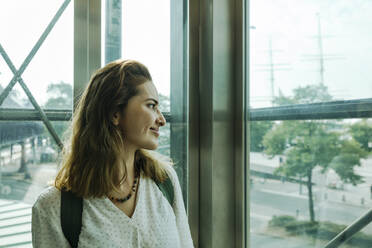 Smiling woman looking through glass in elevator - IHF01259