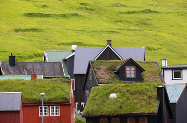 Traditionelle Häuser eines kleinen Dorfes an einem grasbewachsenen Hang auf den Färöer Inseln bei Tageslicht - ADSF38003