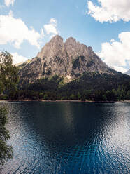 Spektakuläre Landschaft mit ruhigem See, umgeben von massiven grünen Bergen und Nadelbäumen vor blauem Himmel in Aigüestortes i Estany im Nationalpark Saint Maurici - ADSF38013