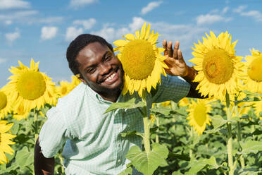 Glücklicher junger Mann posiert mit Sonnenblume im Feld - OSF00922