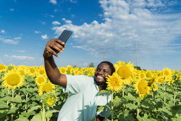 Happy man with sunflower taking selfie through mobile phone in field - OSF00927