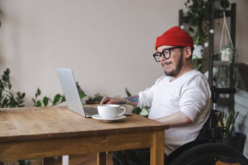 Smiling man in wheelchair using laptop at home - EKGF00016