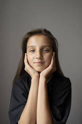 Smiling girl with head in hands against gray background - LESF00185