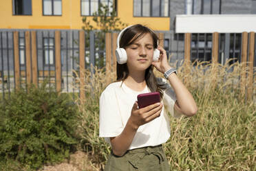 Girl with eyes closed listening music through wireless headphones on sunny day - LESF00201