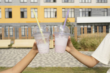 Hände von Mädchen halten Einwegbecher mit Milchshakes vor einem Gebäude an einem sonnigen Tag - LESF00210