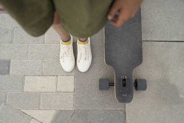 Mädchen steht mit Skateboard auf dem Gehweg - LESF00213