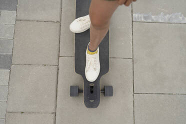 Girl standing on skateboard at footpath - LESF00214