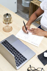 Businesswoman writing in note pad working at home office - VEGF05932