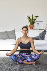 Woman meditating in living room at home - VEGF05940