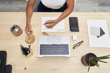 Businesswoman with tea cup writing in note pad at home office - VEGF05950