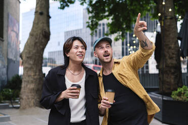 Mann hält Kaffeetasse stehend mit Freund in der Stadt zeigend - ASGF02842