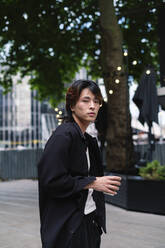 Junger Mann mit Kaffeetasse auf dem Fußweg stehend - ASGF02844