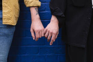 Homosexuelles Paar, das sich an den Händen hält und vor einer blauen Wand steht - ASGF02848