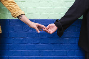 Schwule Männer, die sich an den Händen halten, stehen vor einer Backsteinmauer - ASGF02854