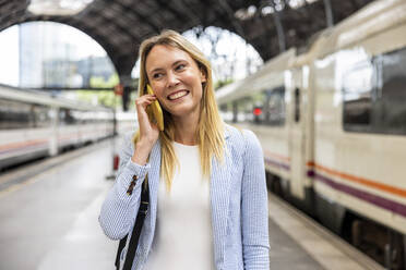 Happy businesswoman talking on smart phone at train station - WPEF06361