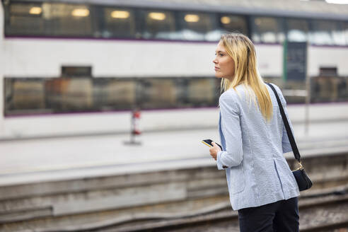 Geschäftsfrau mit blondem Haar wartet am Bahnhof auf einen Zug - WPEF06365