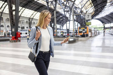 Geschäftsfrau mit Smartphone auf dem Bahnhof - WPEF06366