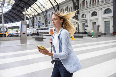 Geschäftsfrau mit Smartphone im Bahnhofsbereich - WPEF06367