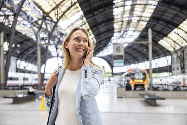 Lächelnde Geschäftsfrau, die am Bahnhof mit einem Smartphone spricht - WPEF06368