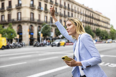 Geschäftsfrau mit erhobener Hand, die eine Mitfahrgelegenheit in der Stadt sucht - WPEF06372