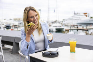 Businesswoman talking on speaker phone sitting at cafe - WPEF06380