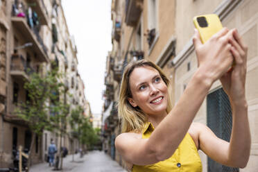 Lächelnde Frau nimmt Selfie durch Smartphone in Gasse - WPEF06384