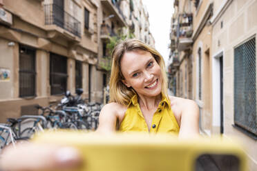 Glückliche Frau nimmt Selfie durch Handy in Gasse - WPEF06385