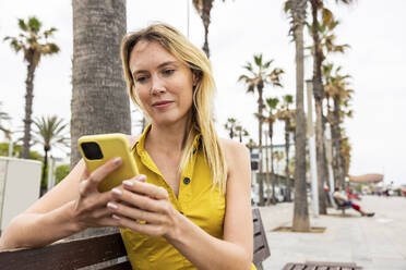Frau mit Smartphone auf einer Bank sitzend - WPEF06399