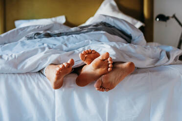 Crop anonyme barfuß Frau und Mann kuscheln Füße beim Schlafen zusammen in weichen Bett zu Hause am Morgen - ADSF38028