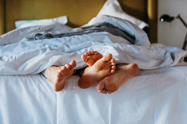 Crop anonymous barefoot wife and husband cuddling feet while sleeping together in soft bed at home in morning - ADSF38028