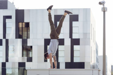 Sportlicher Mann macht Handstand beim Üben von Parkour-Gleichgewichtsübungen im Freien in einer städtischen Szene - ADSF38067