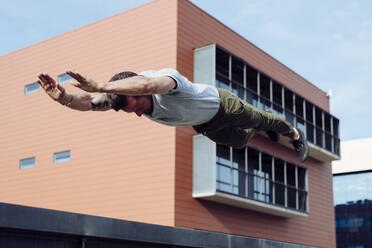 Athletischer Mann macht Parkour-Übung im Freien springen mit den Händen in der Luft - ADSF38070