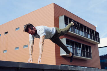 Athletic man doing parkour exercise outdoors jump with hands in the air - ADSF38071