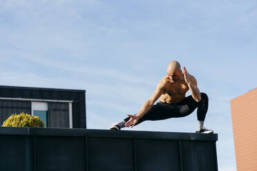 Sportlicher Mann macht Parkour-Gleichgewichtsübungen im Freien in einer städtischen Szene - ADSF38073