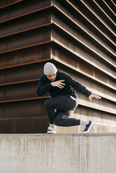 Athletic man doing parkour balance exercises outdoors in urban scene - ADSF38079