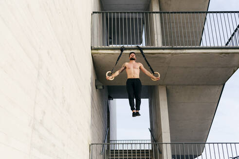 Young shirtless sportsman balancing on gymnastic rings outdoors - ADSF38084