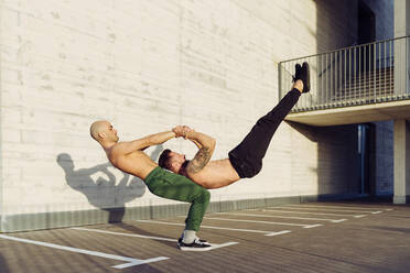 Young athletic shirtless men doing an urban workout outdoors practicing balance exercises - ADSF38087