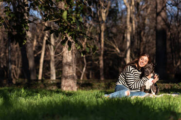 Junge Frau, die Spaß mit ihrem amerikanischen Stanford-Hund hat, während sie auf dem Gras im Park sitzt - ADSF38111