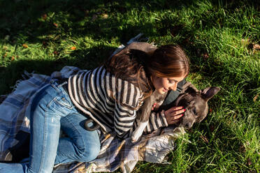 Young woman having fun with her american stanford dog while lying down on grass at park - ADSF38112