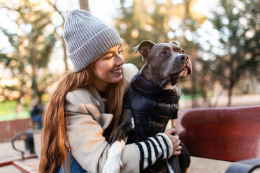 Junge Frau hat Spaß mit ihrem amerikanischen Stanford-Hund, während sie auf einer Bank im Park sitzt - ADSF38115