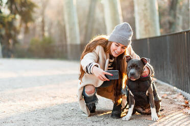 Junge Frau macht ein Selfie mit ihrem amerikanischen Stanford-Hund beim Spaziergang im Park - ADSF38116