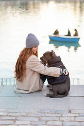 Rückenansicht einer jungen Frau, die sich mit ihrem amerikanischen Stanford-Hund in der Nähe eines Sees vergnügt - ADSF38123