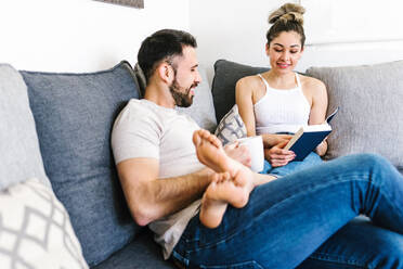 Content ethnic couple sitting on sofa together relaxing at weekend at home - ADSF38148