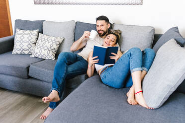 Content ethnic couple sitting on sofa together while looking at each other and relaxing at weekend at home - ADSF38149