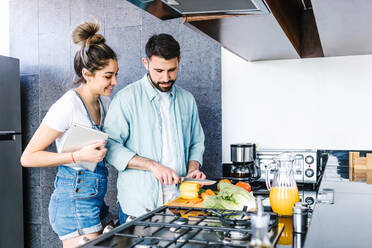 Begeistertes lateinamerikanisches Paar, das frisches reifes Gemüse schneidet und einen gesunden Salat für das Mittagessen in der Küche zu Hause zubereitet und sich dabei gegenseitig ansieht - ADSF38183