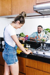 Side view of smiling Latin couple preparing fresh vegetable salad for healthy lunch in kitchen - ADSF38190