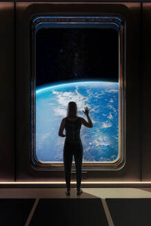 Female astronaut saying goodbye through Earth's window on her mission to Mars trip - ADSF38200